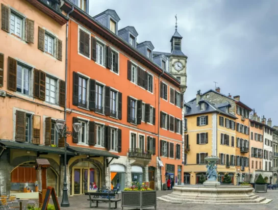 Vue pittoresque de la Place Saint-Léger à Chambéry, avec ses façades colorées, ses volets en bois et sa fontaine emblématique, en plein cœur de la Savoie