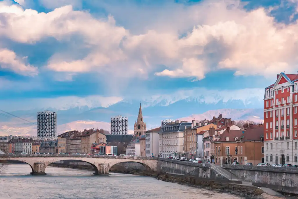 Vue pittoresque de Grenoble avec la rivière Isère, le pont, l’église Saint-André et les montagnes des Alpes en arrière-plan.