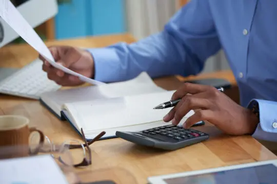 Homme en chemise bleue travaillant sur un rapport financier avec une calculatrice, un stylo et des documents sur un bureau