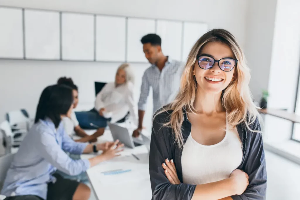 Femme souriante au premier plan, avec une équipe collaborant et échangeant sur un projet en arrière-plan.