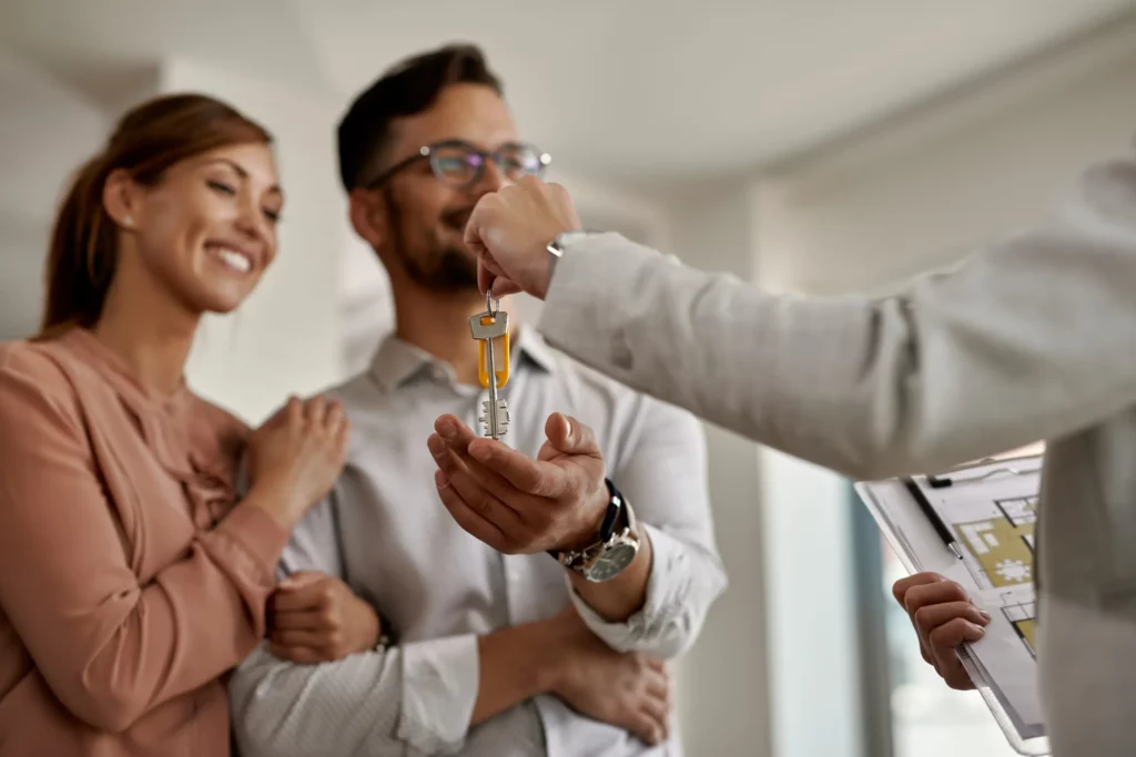 Gros plan sur une agente immobilière remettant les clés d’une nouvelle maison à un couple, illustrant la formation professionnelle Ecoris en immobilier.