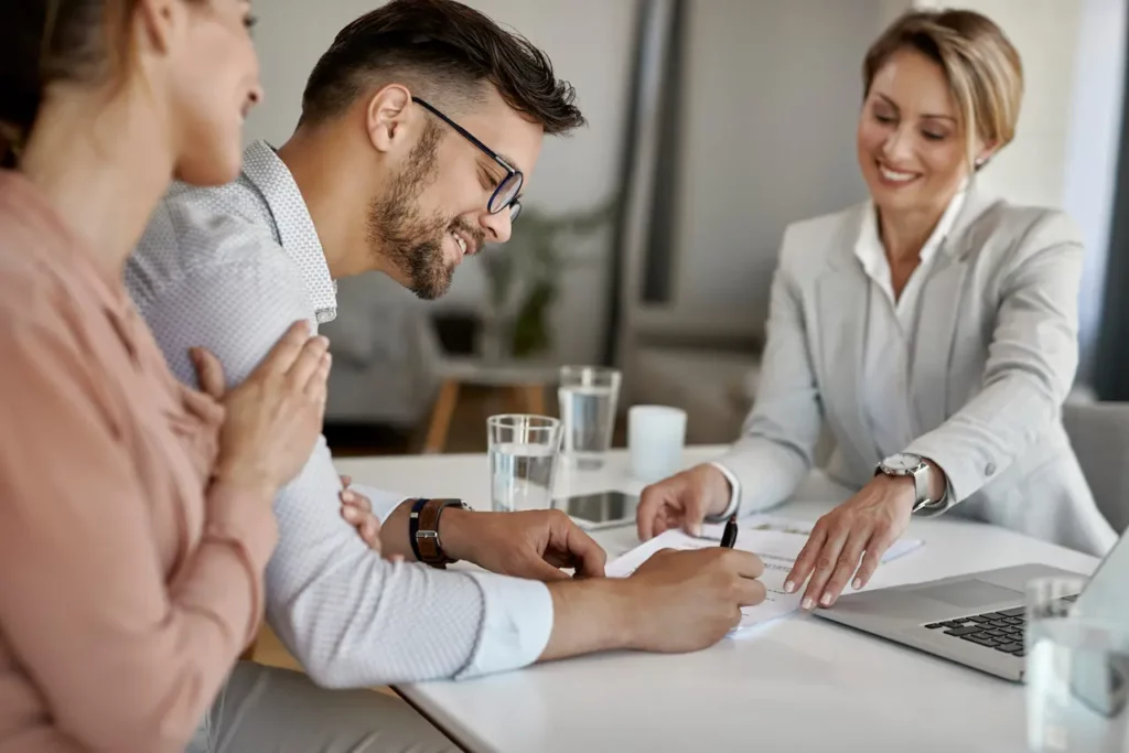 Femme faisant signer un contrat à un couple, conclusion d’un accord professionnel.