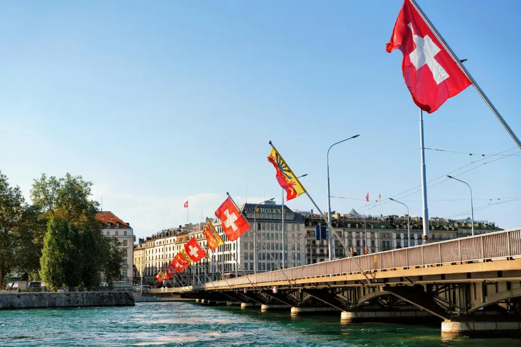 Pont du Mont-Blanc à Genève, décoré de drapeaux suisses et genevois, surplombant le Rhône par une journée ensoleillée.