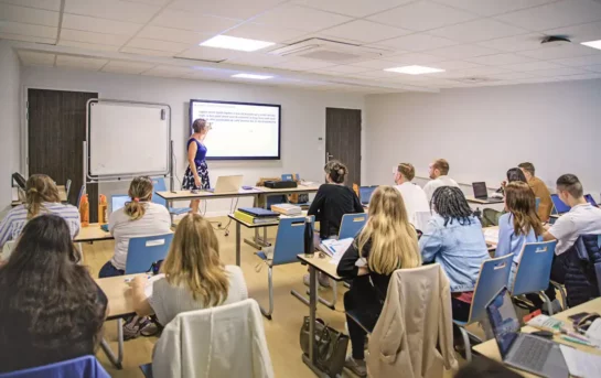 Une salle de classe au campus Ecoris de Mâcon, avec une formatrice donnant un cours projeté sur un écran et des étudiants attentifs prenant des notes